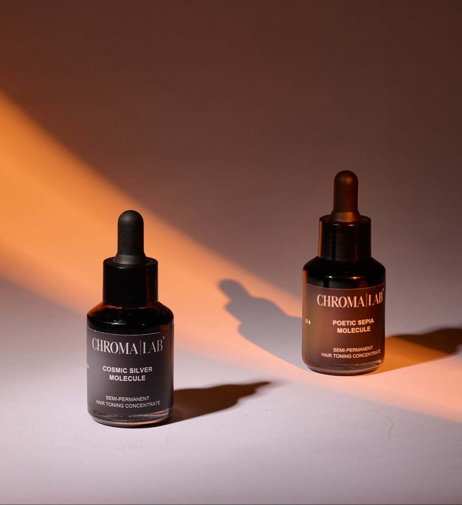 Two bottles of Chromalab Molecules hair toning concentrated on a gradient background with warm lighting.