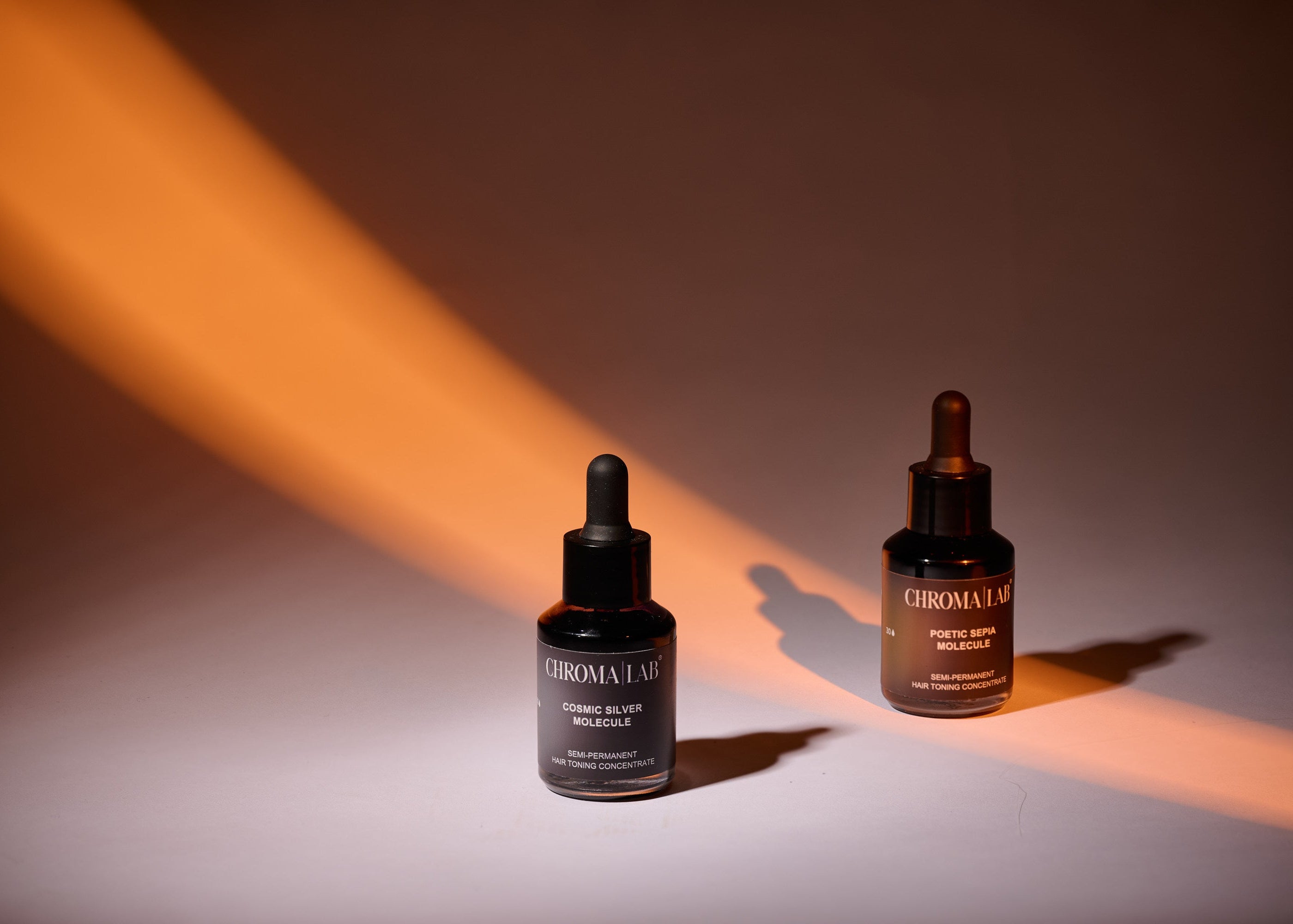 Two bottles of Chromalab Molecules hair toning concentrated on a gradient background with warm lighting.