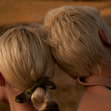 Close-up of a person with blonde hair tied back with a green scrunchie against a blurred background