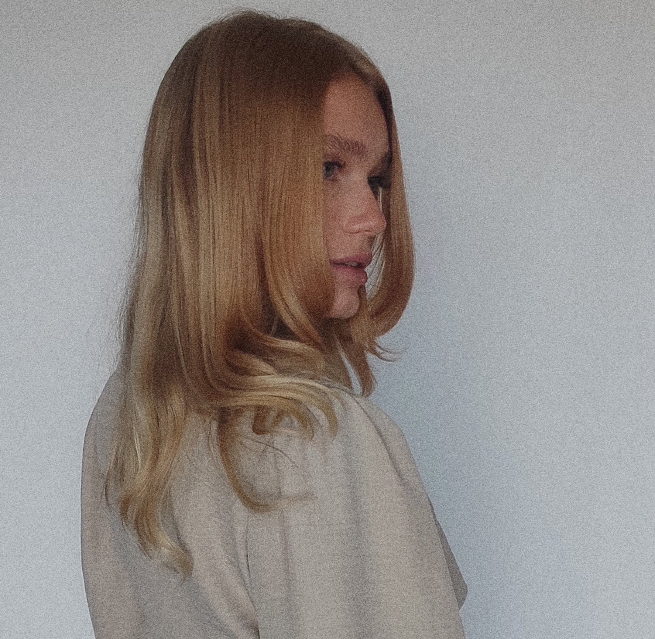 Woman with long blonde hair wearing a beige sweater against a plain background