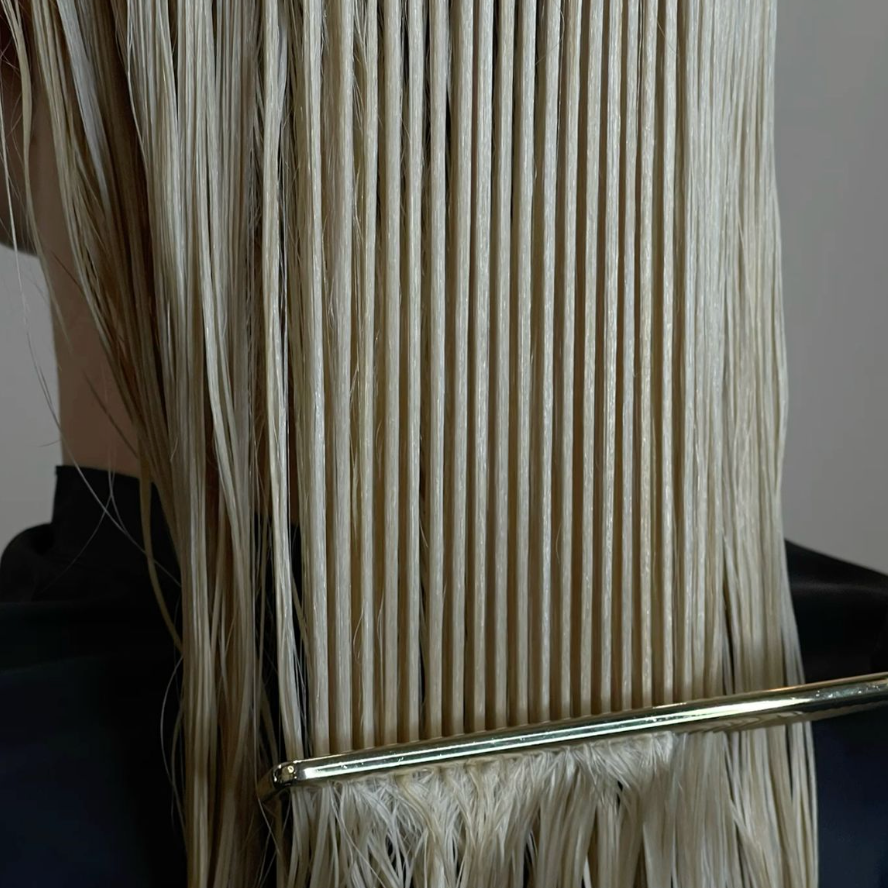 Close-up of a hair extension with a clear plastic cover on a neutral background